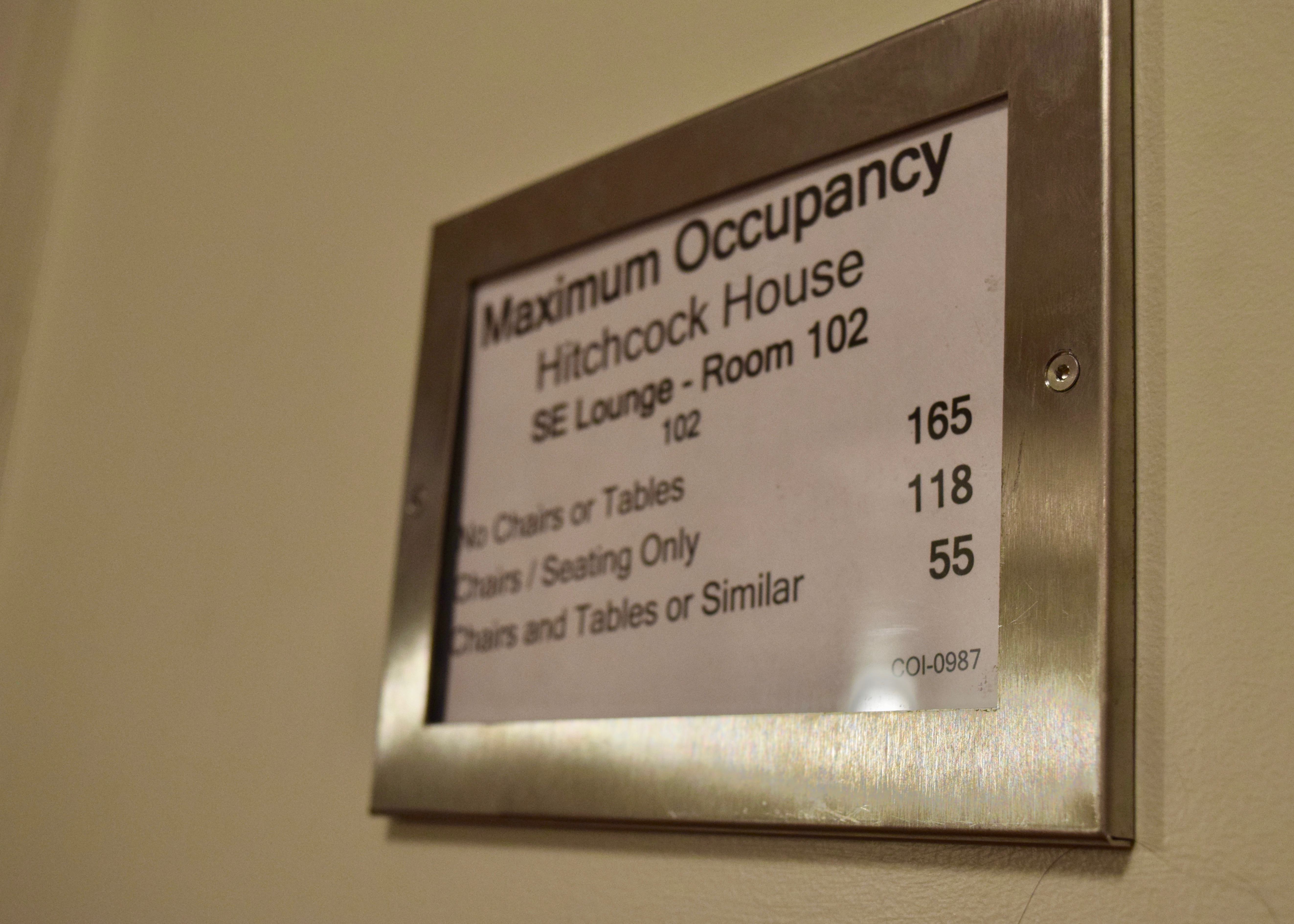 A frame on the wall posts the maximum occupancy in the SE Lounge, or Room 102, for Hitchcock House: "No Chairs or Tables — 165," "Chairs/Seating Only — 118" and "Chairs and Table or Similar — 55."